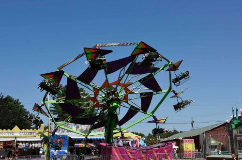A colorful amusement park ride spins against a clear blue sky, with people enjoying the thrill.