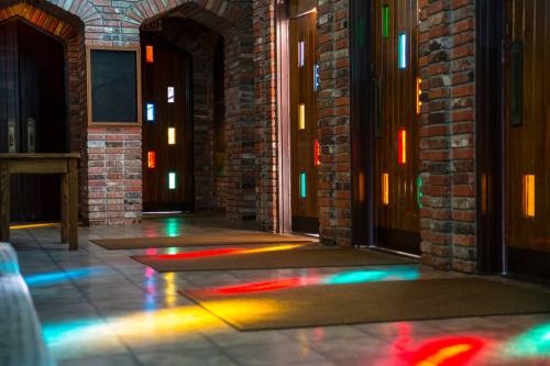 A hallway with brick walls and colorful light reflections on the floor from stained glass windows.