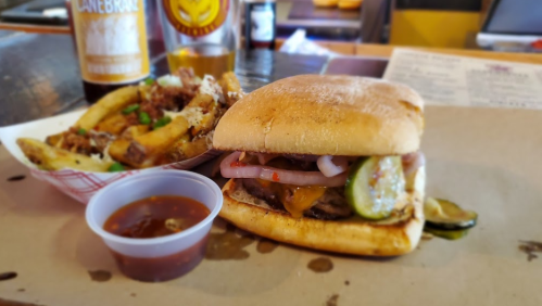 A juicy burger with pickles and onions, served with fries and a small cup of dipping sauce.