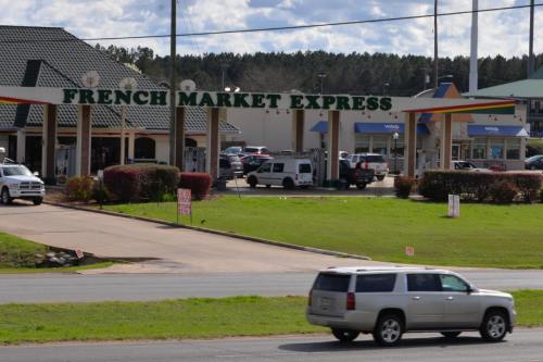 A view of French Market Express with a parking lot and a car driving by on a sunny day.