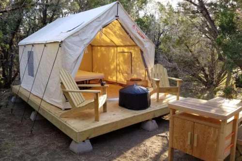 A cozy glamping tent on a wooden platform, surrounded by trees, with chairs and a small table outside.