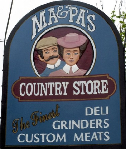 Sign for "Ma & Pa's Country Store" featuring a man and woman, advertising deli, grinders, and custom meats.