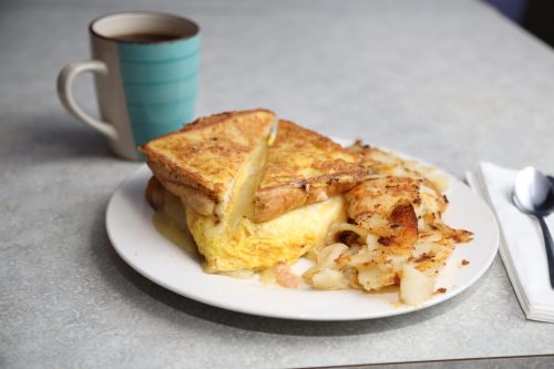 A plate with a fluffy omelet, French toast, crispy hash browns, and a cup of coffee on a table.