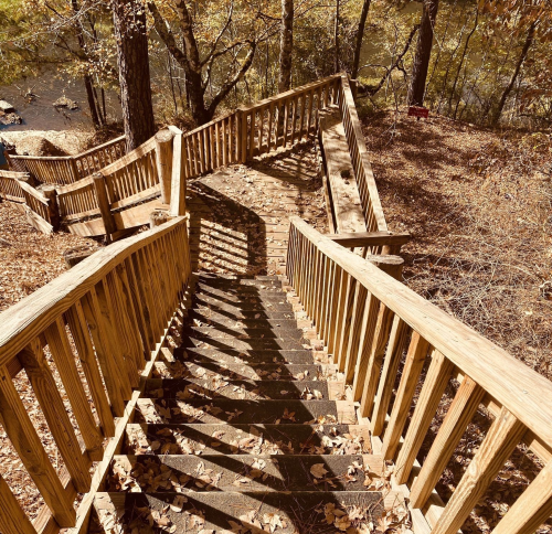 Wooden staircase winding down through autumn foliage, leading to a serene body of water below.