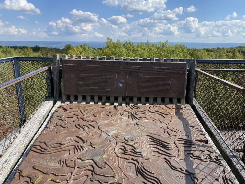 View from an observation deck featuring a textured map and informational plaques, surrounded by greenery and blue skies.