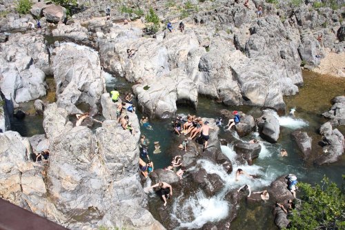 A rocky river area filled with people swimming and relaxing among the boulders on a sunny day.