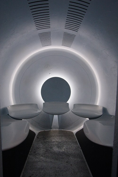A minimalist, circular room with soft lighting and curved seating around a central circular feature.