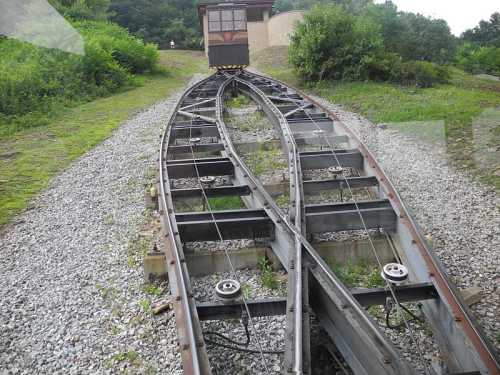 A view of railway tracks diverging in a green landscape, leading to a wooden train car on a hill.