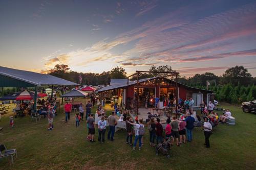 A lively outdoor gathering at sunset, with people socializing near a rustic building and colorful tents.