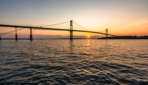 A sunset view of a bridge spanning over calm waters, with vibrant colors in the sky reflecting on the surface.