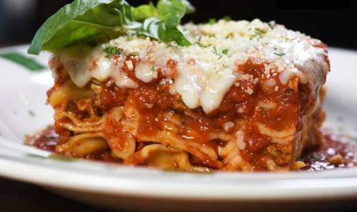A close-up of a delicious lasagna topped with melted cheese, marinara sauce, and fresh basil on a white plate.