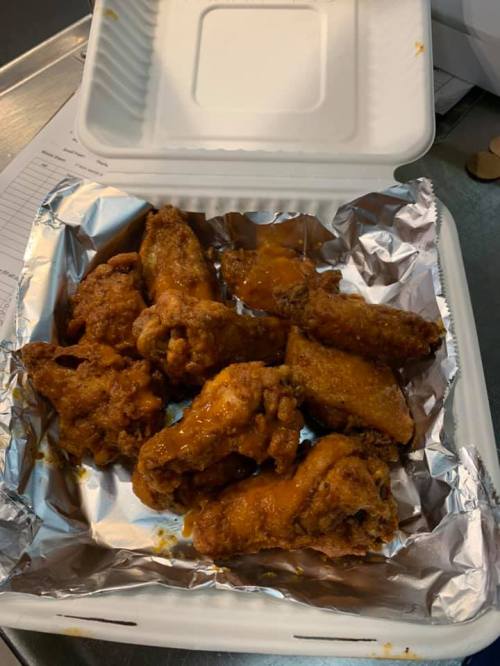 A takeout container filled with crispy, sauced chicken wings on a bed of foil.