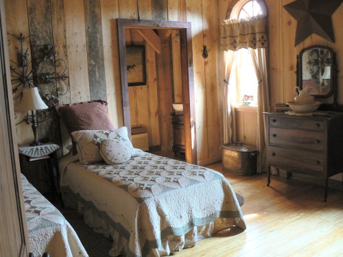 Cozy bedroom with two twin beds, wooden walls, a large mirror, and vintage decor. Natural light from a window.