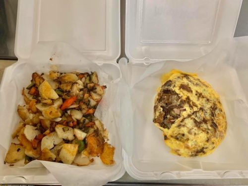 A takeout container with seasoned potatoes on one side and a hearty omelette filled with meat on the other.