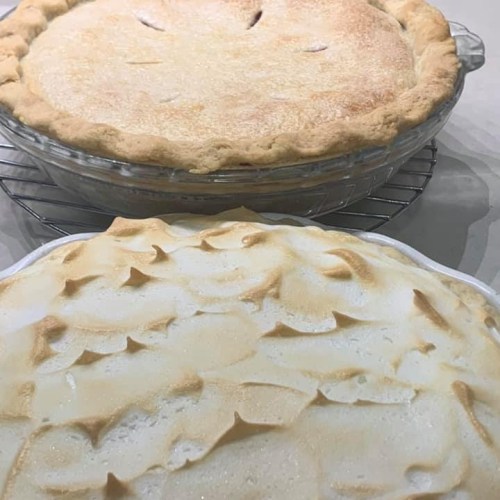 A freshly baked apple pie on a cooling rack, with a meringue-topped pie in the foreground.