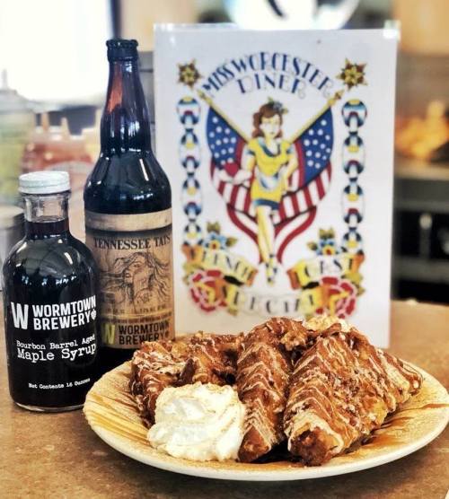 A plate of crispy fried chicken with a side of whipped cream, accompanied by bottles of maple syrup and soda, and a diner menu.