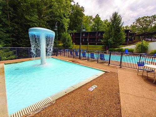 A pool area featuring a waterfall fountain, lounge chairs, and surrounded by trees and a building in the background.