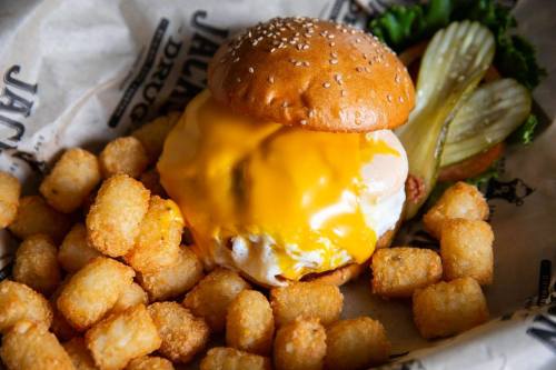 A cheeseburger with melted cheese and pickles, served with crispy tater tots on a paper-lined tray.