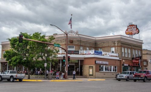 Historic building with "Irma Hotel" sign, American flag, and people outside on a cloudy day. Cars at the intersection.