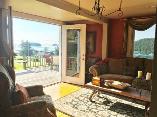 Cozy living room with a view of a deck and scenic landscape through open doors, featuring comfortable furniture and decor.