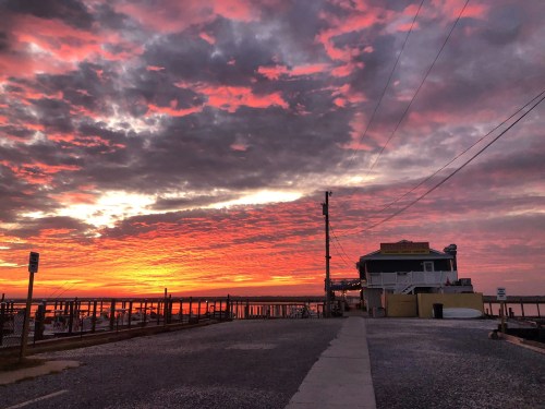 A vibrant sunset paints the sky in shades of pink and orange over a waterfront building and pier.