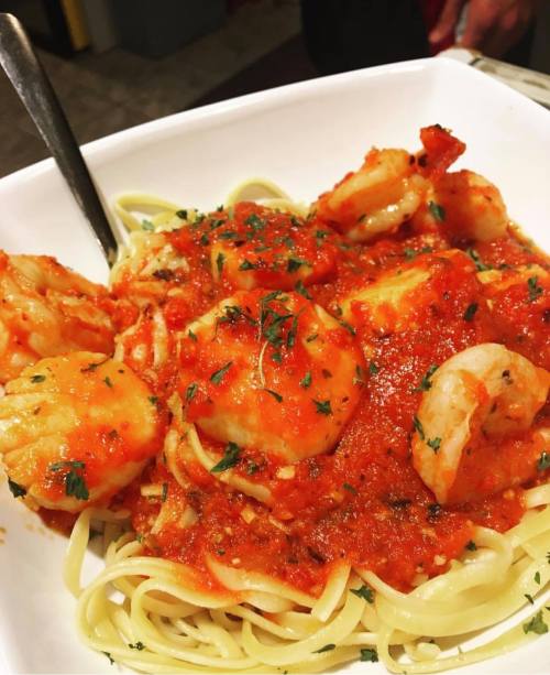 A bowl of pasta topped with shrimp in a rich red sauce, garnished with herbs.