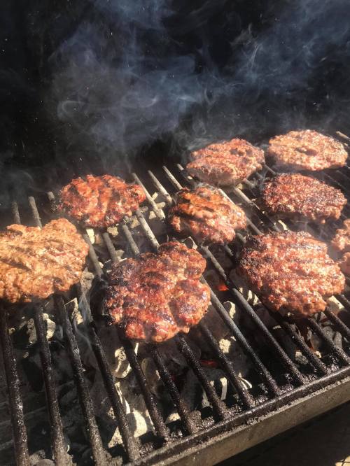 Grilling burgers on a barbecue, with smoke rising and patties sizzling on the grill.