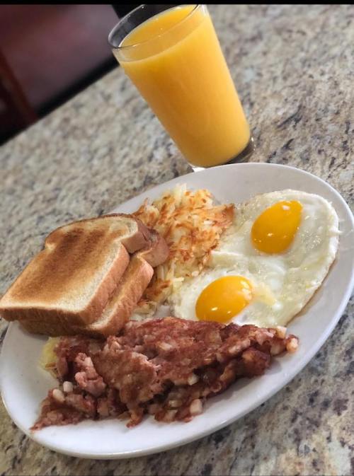 A plate of breakfast with two fried eggs, hash browns, sausage, toast, and a glass of orange juice.