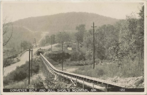 Black and white image of a conveyor belt leading to Bull Shoals Mountain, with trees and power lines in the background.