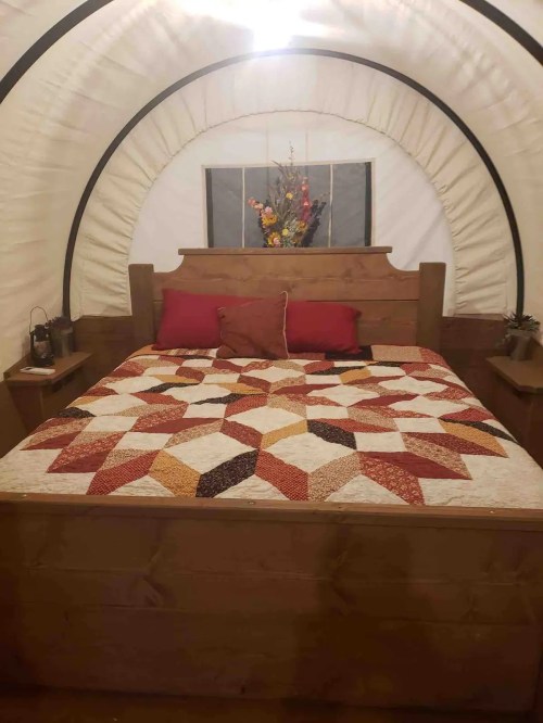 Cozy bedroom with a wooden bed, colorful quilt, and decorative flowers in a curved, tent-like space.