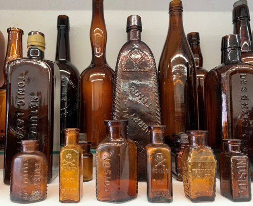 A collection of vintage amber glass bottles of various shapes and sizes displayed on a shelf.