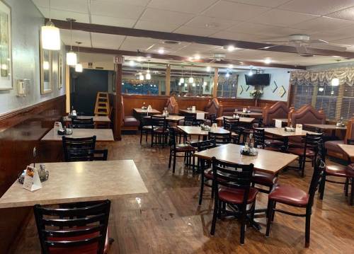 A cozy restaurant interior with empty tables, wooden floors, and warm lighting.