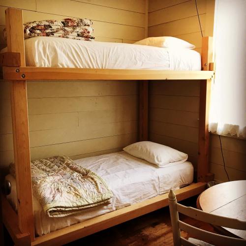 A wooden bunk bed with a top and bottom mattress, a quilt on the bottom, and a small table nearby in a cozy room.