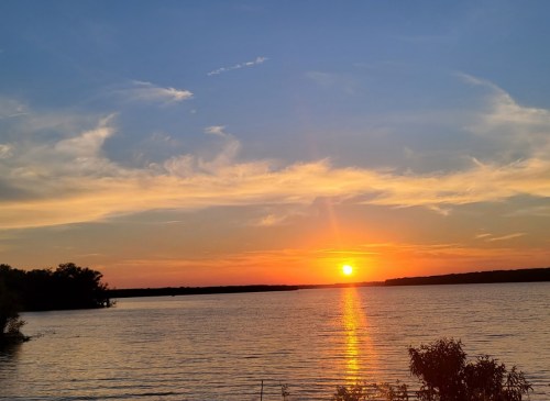 A serene sunset over a calm lake, with vibrant orange and blue hues reflecting on the water.