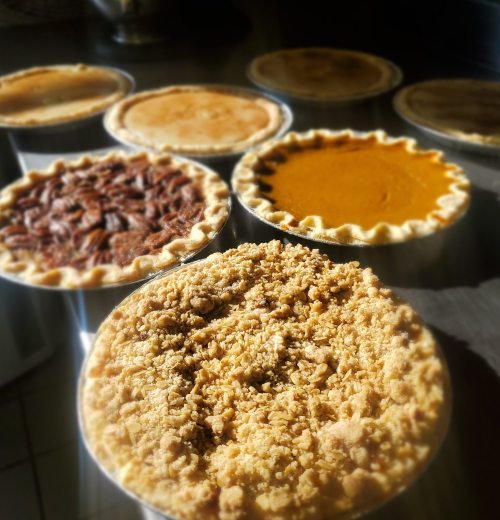 A variety of freshly baked pies, including pecan, pumpkin, and crumb-topped, arranged on a countertop.