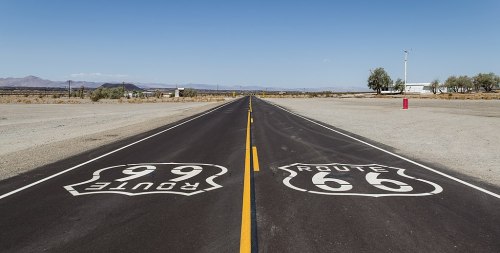 A wide, empty road with Route 66 and Route 99 signs painted on the pavement, surrounded by a desert landscape.