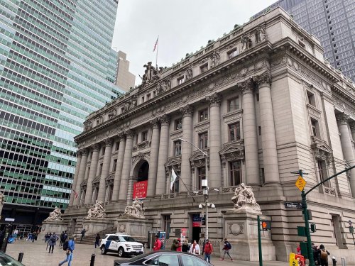 Historic building with ornate architecture, surrounded by modern skyscrapers and bustling city streets.