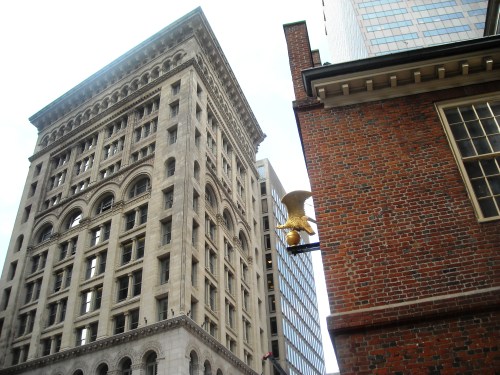 View of a historic building with ornate architecture next to a brick structure, featuring a golden eagle sculpture.