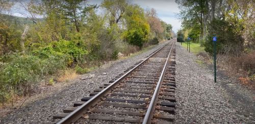 A view of a railway track stretching into the distance, flanked by trees and greenery on both sides.