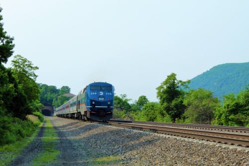 A train approaches a tunnel along a scenic railway surrounded by greenery and hills.
