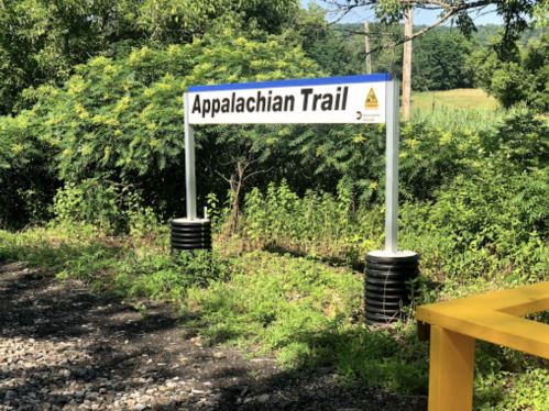 Sign for the Appalachian Trail surrounded by greenery and trees, with a clear blue sky in the background.