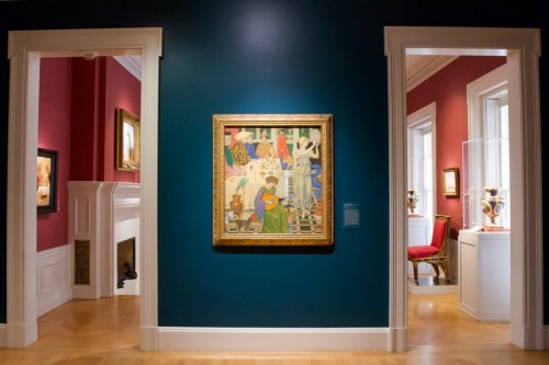 A colorful painting hangs on a teal wall in an art gallery, flanked by red walls and visible artworks in adjacent rooms.