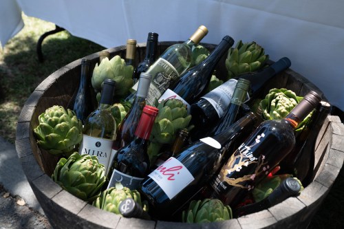 A wooden barrel filled with various wine bottles surrounded by artichokes.