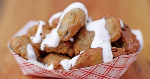 A basket of crispy fried snacks drizzled with creamy white sauce, set on a wooden surface.