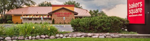A restaurant building with a colorful exterior and a sign reading "Bakers Square" surrounded by greenery and flowers.