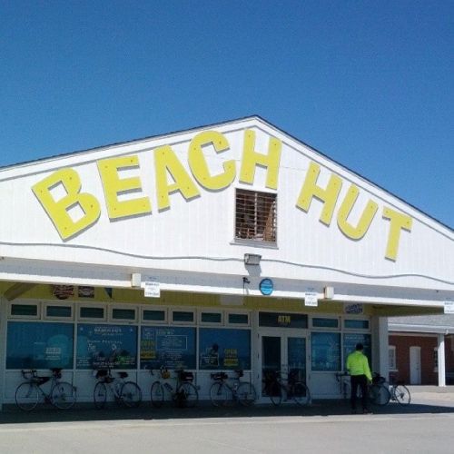 A bright blue sky above a building with "BEACH HUT" in large yellow letters and bicycles parked outside.