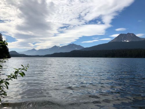 A serene lake surrounded by mountains under a partly cloudy sky, reflecting the landscape on the water's surface.