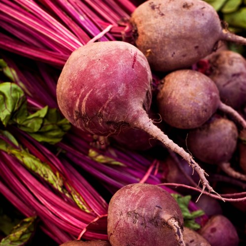 A close-up of fresh beets with vibrant green leaves, showcasing their earthy tones and textures.