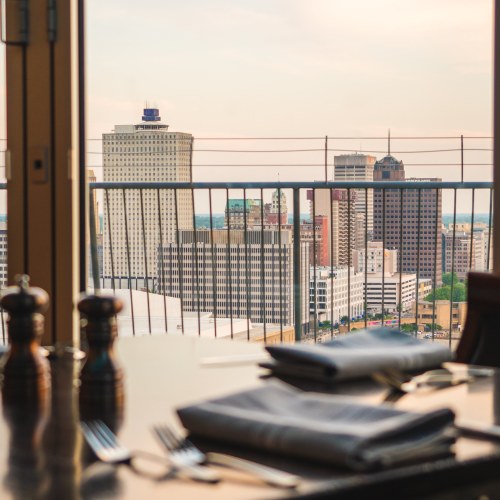 A city skyline view from a restaurant table, featuring buildings and a sunset in the background.