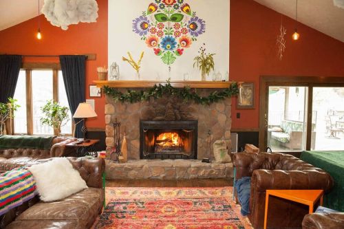 Cozy living room with a stone fireplace, colorful wall art, leather sofas, and a vibrant rug. Warm and inviting atmosphere.